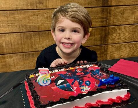Elementary aged boy sitting posing for a picture with his red and blue birthday cake