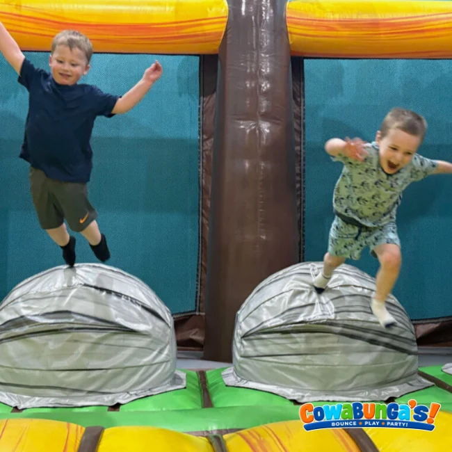 Two children jumping on inflatable obstacles at Cowabunga’s in Manchester, NH