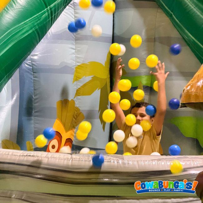 Child on an inflatable slide with colorful balls at Cowabunga’s Manchester, NH